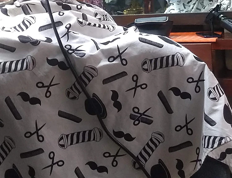Capa blanca estampada con postes de barbero, tijeras, peines y bigotes en negro