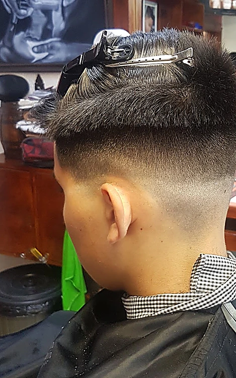 Degradado alto visto desde la nuca, con el cabello de arriba sujeto con una pinza y la capa negra puesta