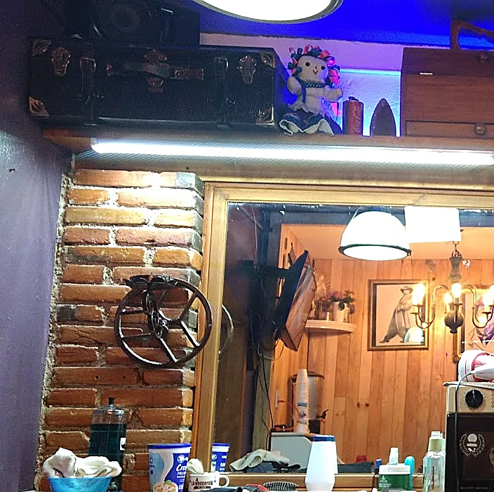 Estación de trabajo con columna de ladrillo, espejo de marco dorado, luz azul-violeta en la repisa, baúles antiguos y una muñeca de trapo