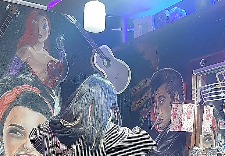 Mural pintado de pin-ups tatuadas en rojo y negro, una guitarra morada colgada y la luz violeta del techo