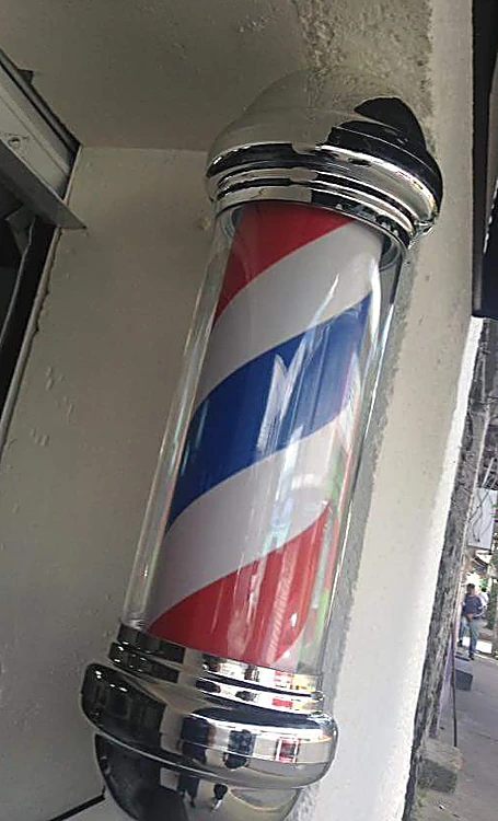 Poste de barbero cromado con franjas rojas, blancas y azules en la fachada